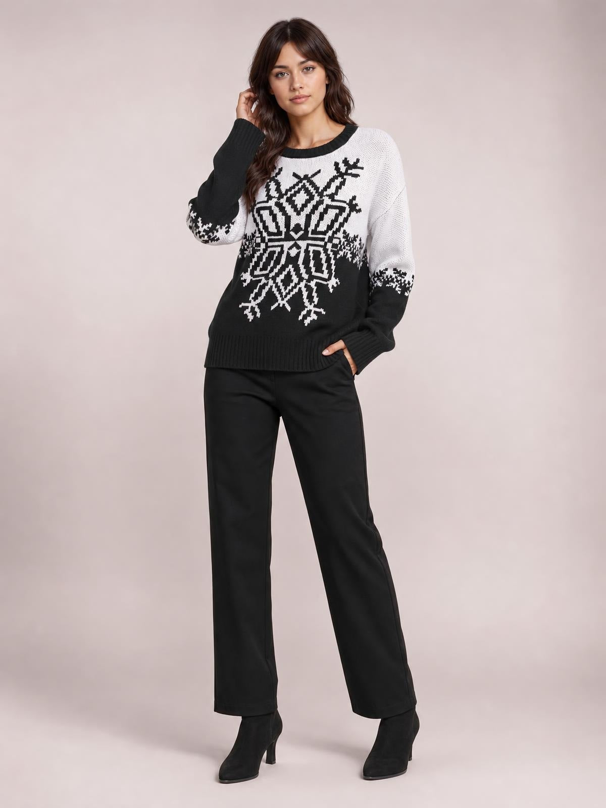 Model wears a black-and-white Christmas snowflake sweater with a round neck, long sleeves, ribbed cuffs and hem, and a relaxed silhouette, posing with one hand in a pocket.