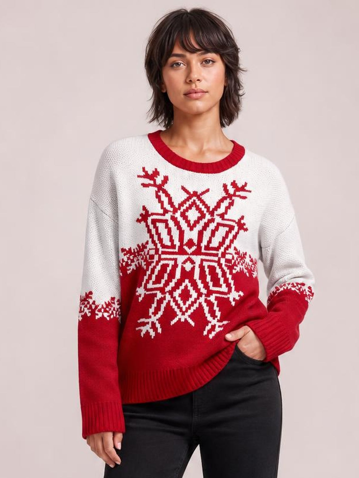 Model wears a relaxed white and red Christmas snowflake sweater with a ribbed round neck, cuffs, hem, and long sleeves, posing with one hand in her pocket.