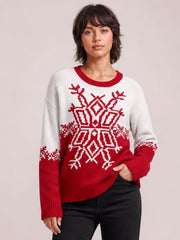 Model wears a relaxed white and red Christmas snowflake sweater with a ribbed round neck, cuffs, hem, and long sleeves, posing with one hand in her pocket.
