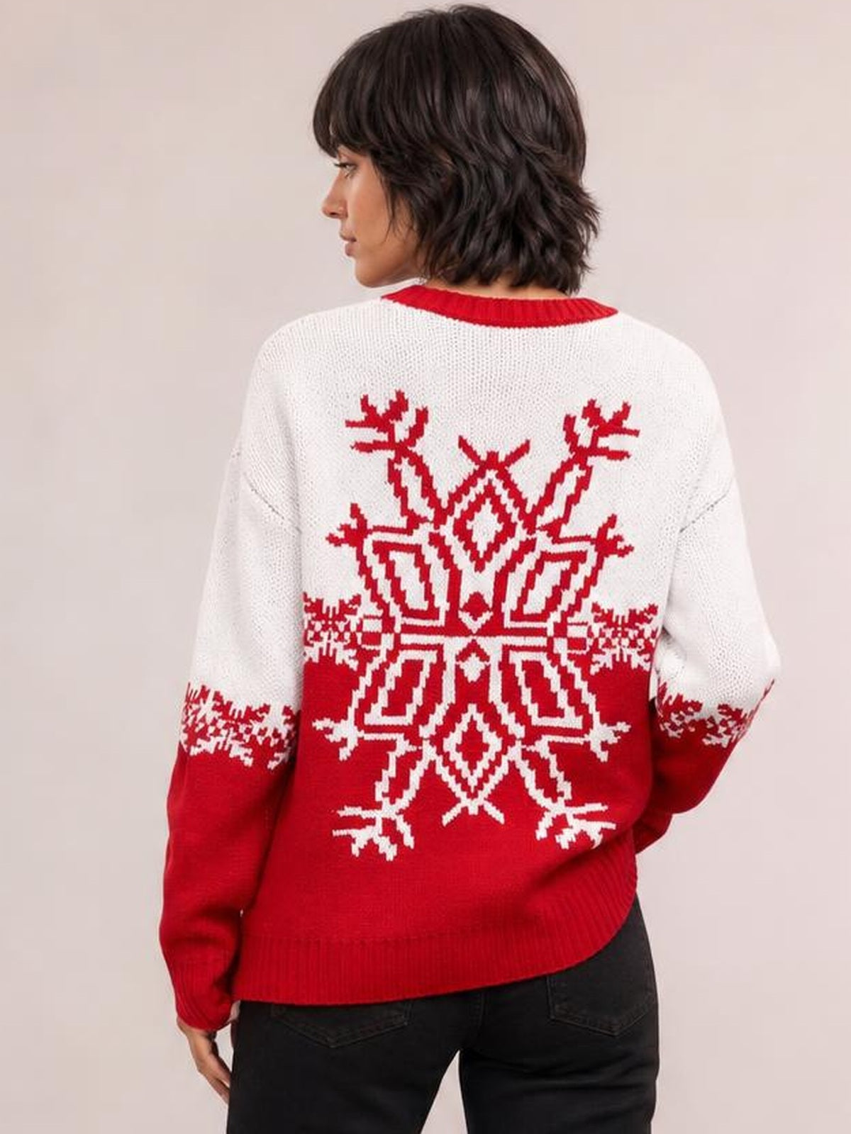 Model turned away displays a red and white Christmas snowflake sweater with a round neck, long sleeves, relaxed silhouette, and ribbed cuffs and hem.