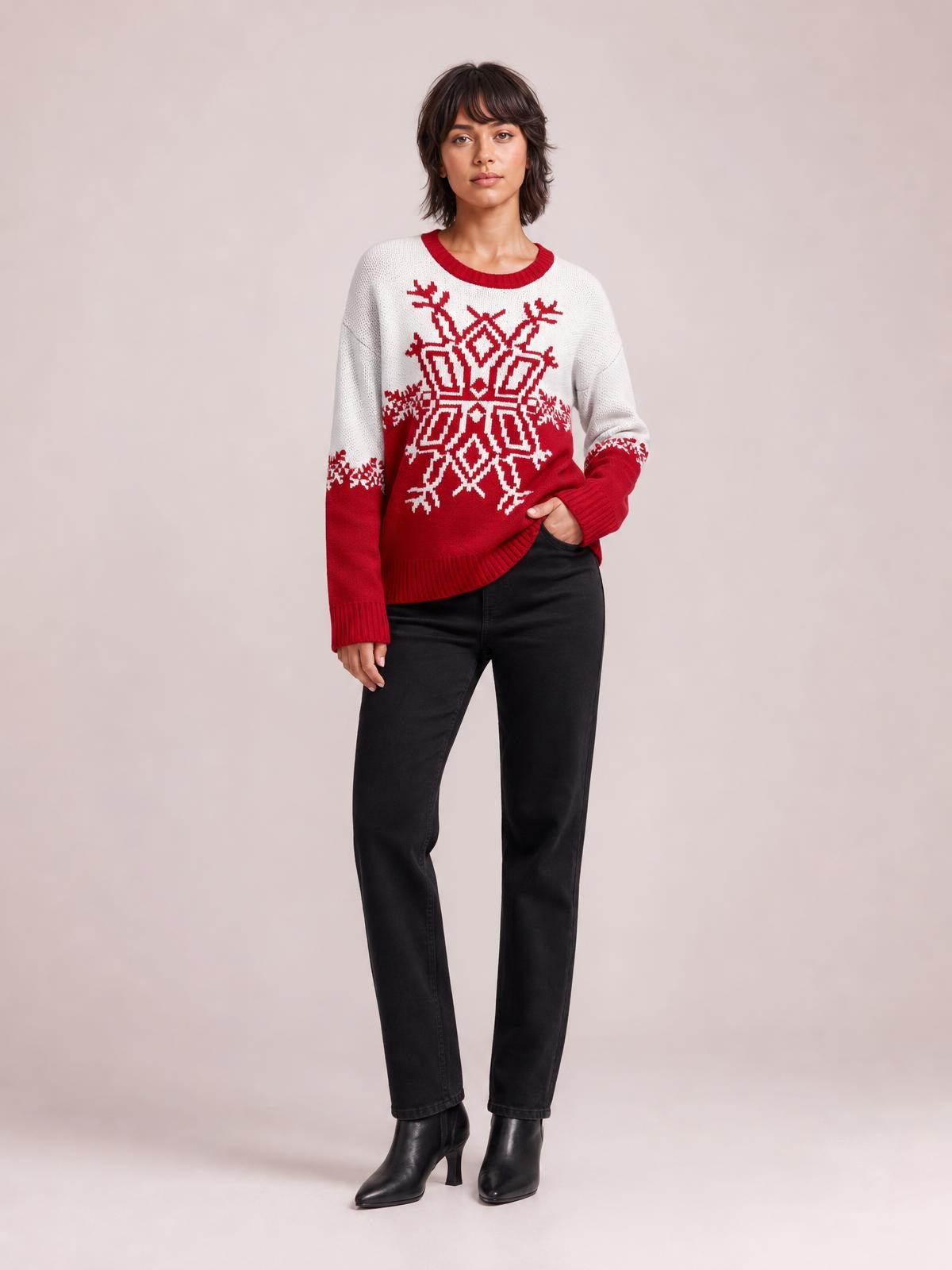Model wearing a red and white Christmas snowflake round neck sweater with a relaxed silhouette, ribbed cuffs and hem, standing with one hand in her pocket.