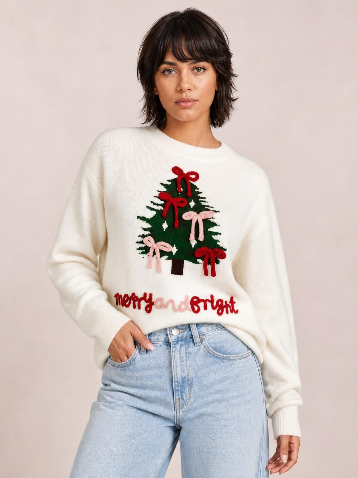 Model wears an ivory Christmas tree bow drop-shoulder knit sweater with a relaxed silhouette, crew neck, ribbed cuffs, and colorful tree appliqué.