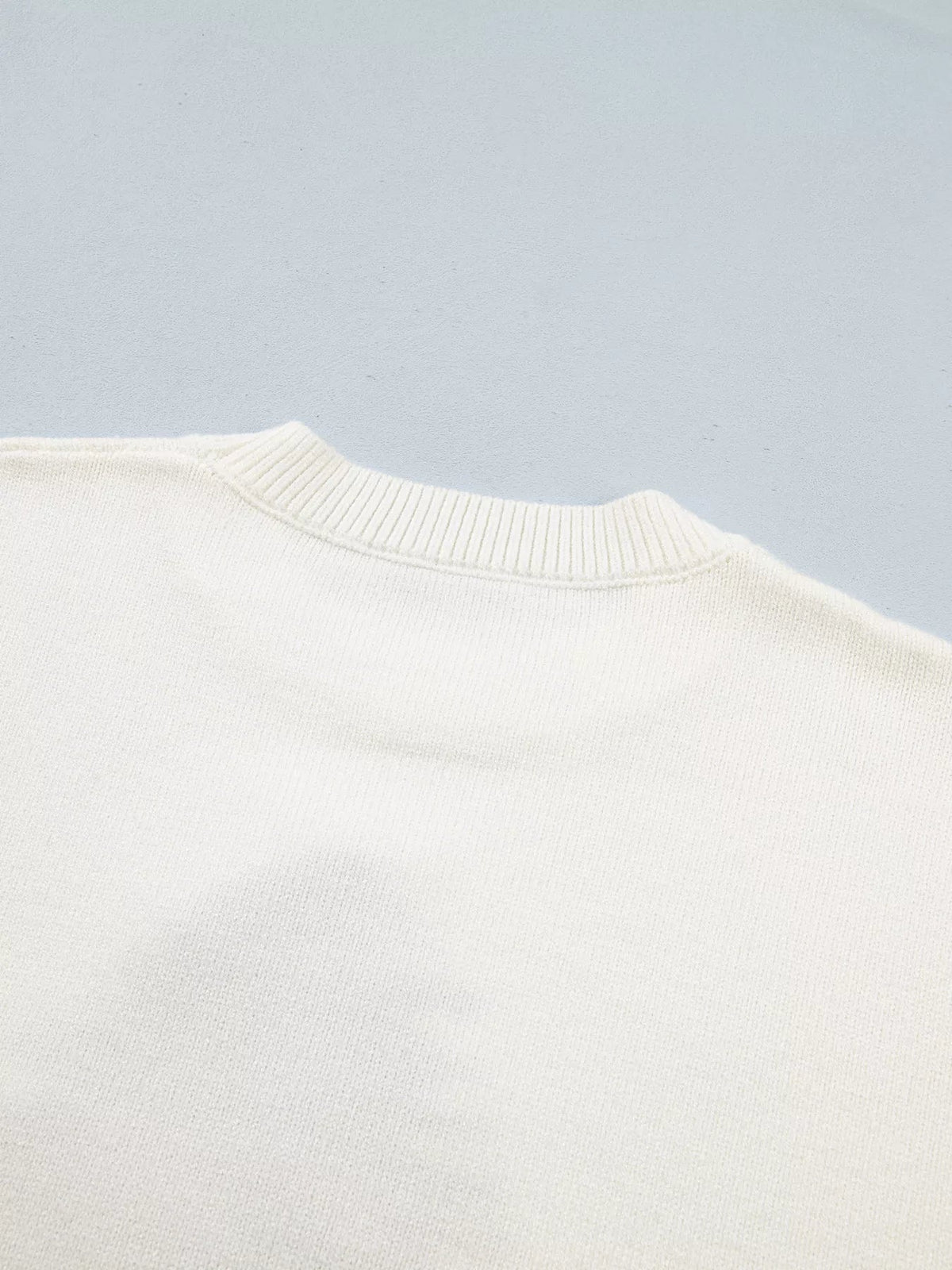 Close-up of an ivory knit sweater showing its softly textured stretch fabric, ribbed crew neckline, and clean basic construction.
