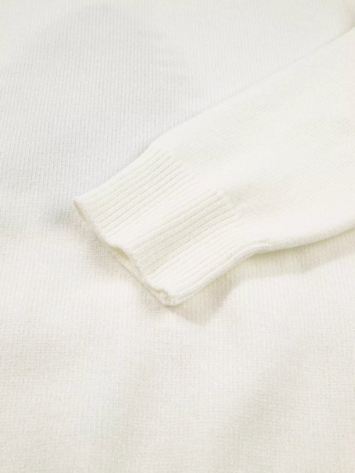 Close-up of an ivory knit sweater sleeve showing a soft textured knit and wide ribbed cuff construction.