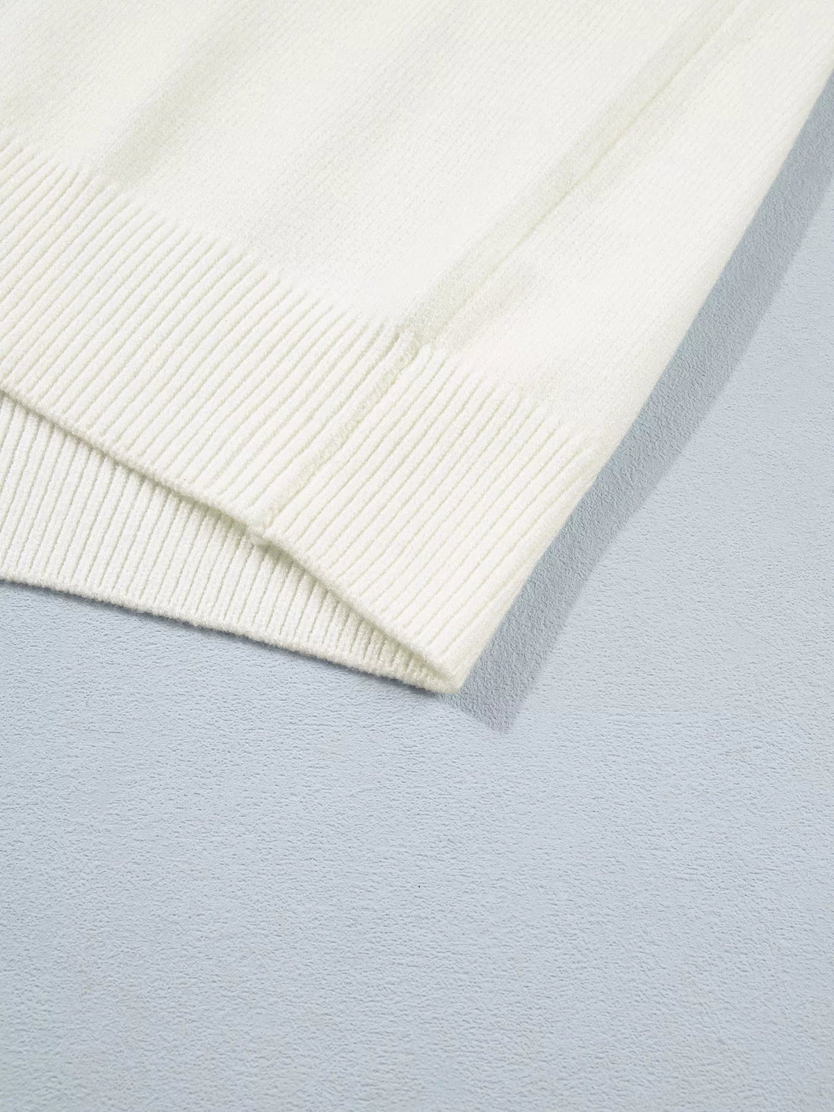 Close-up of an ivory knit sweater showing its soft textured fabric and neatly finished ribbed hem or cuff.