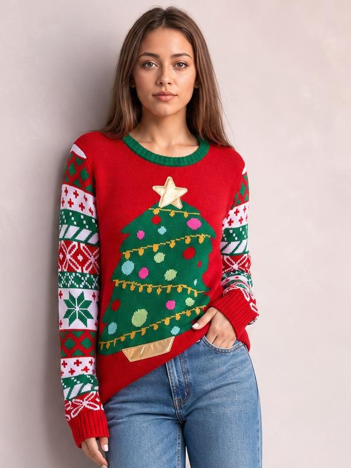 Model poses in a red Christmas tree graphic round neck sweater with green trim, patterned long sleeves, ribbed cuffs, and a relaxed straight silhouette.