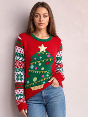 Model poses in a red Christmas tree graphic round neck sweater with green trim, patterned long sleeves, ribbed cuffs, and a relaxed straight silhouette.