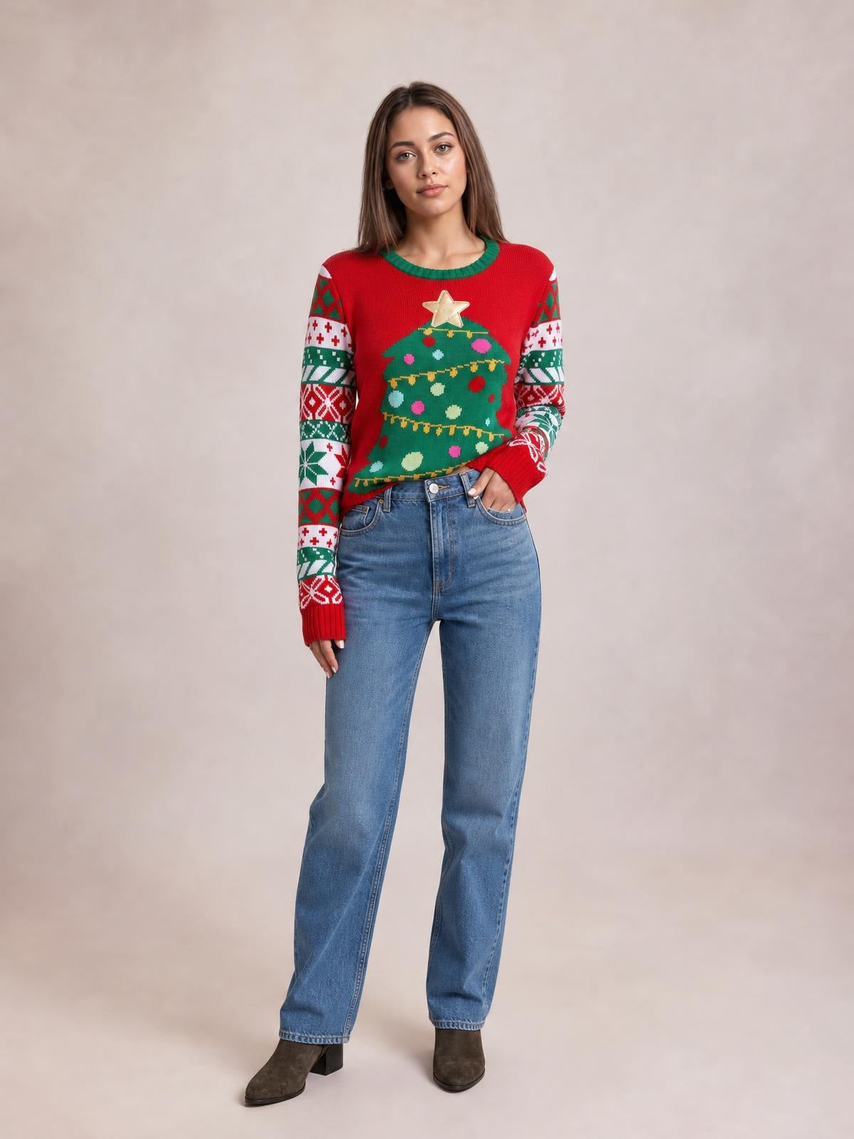 Model wearing a red Christmas tree graphic round neck sweater with green trim, patterned long sleeves, ribbed cuffs, and a relaxed silhouette, posing with one hand in her jeans pocket.