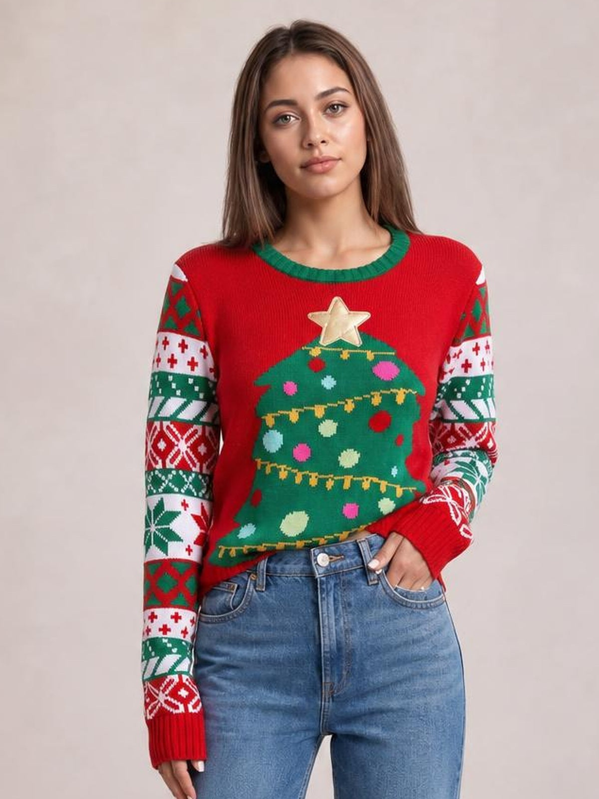 Model poses with one hand in her jeans pocket, wearing a red round-neck Christmas tree graphic sweater with festive patterned sleeves and a relaxed silhouette.