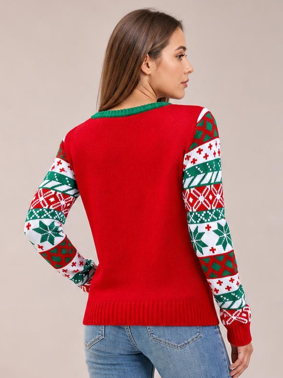 Back view of a model wearing a red Christmas sweater with a green round neckline, patterned long sleeves, ribbed cuffs and hem, posing with one hand on her hip.