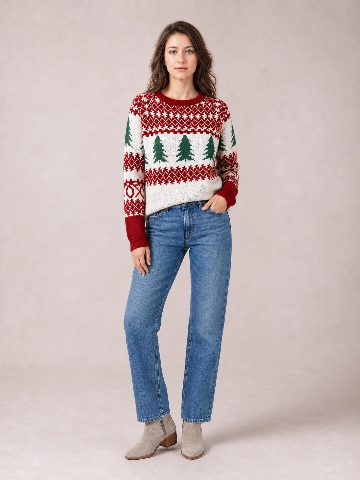 A woman models a red, white, and green Christmas tree pattern round-neck sweater with ribbed cuffs and hem in a relaxed silhouette, one hand in her jeans pocket.