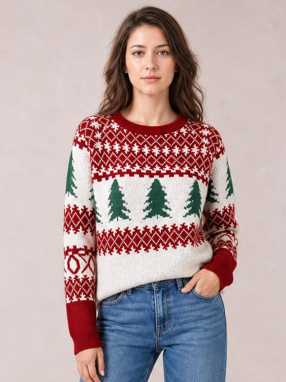 Model wearing a red, white, and green Christmas tree pattern round neck sweater with long sleeves, ribbed trim, and a relaxed silhouette, posing with one hand in her jeans pocket.