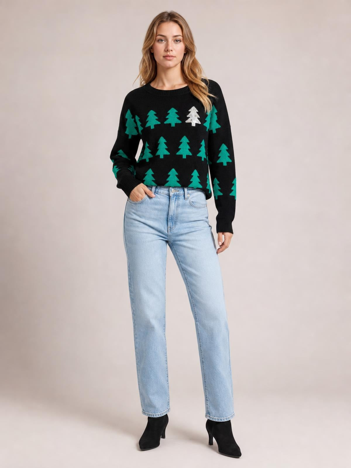 Model poses with one hand in her jeans pocket, wearing a black Christmas tree patterned sweater with a round neck, ribbed trim, long sleeves, and a regular silhouette.