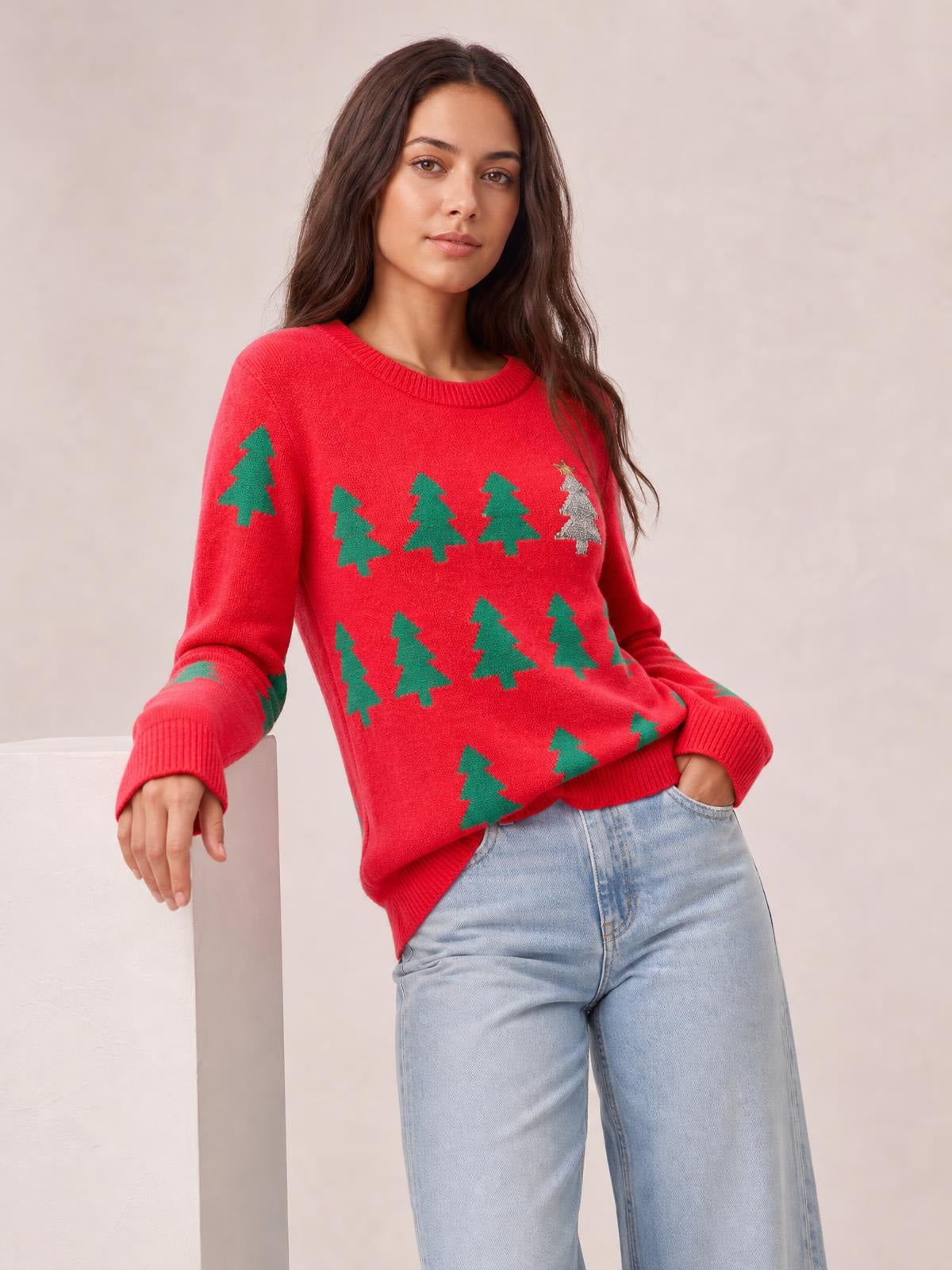 A model poses in a red Christmas tree sweater with green tree motifs, a round neck, ribbed trim, long sleeves, and a relaxed regular-length silhouette.