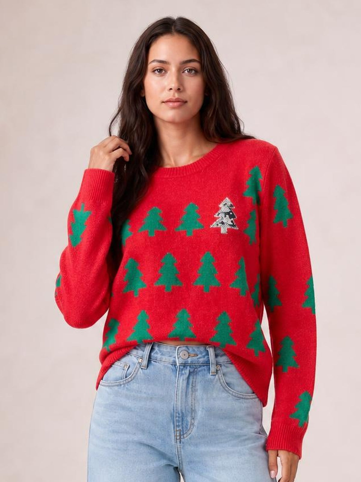 Model wearing a red Christmas tree sweater with a round neck, ribbed trim, long sleeves, regular silhouette, and green tree motifs while touching her hair.