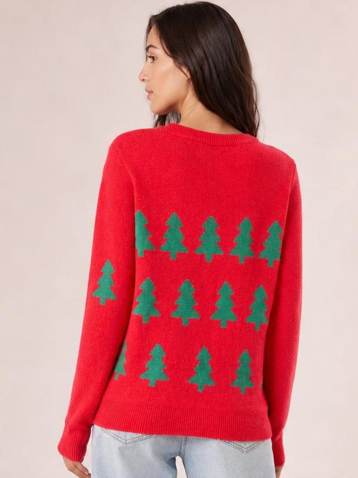 Model turned away to show a red Christmas tree sweater with green tree pattern, round neckline, long regular sleeves, and ribbed trim.