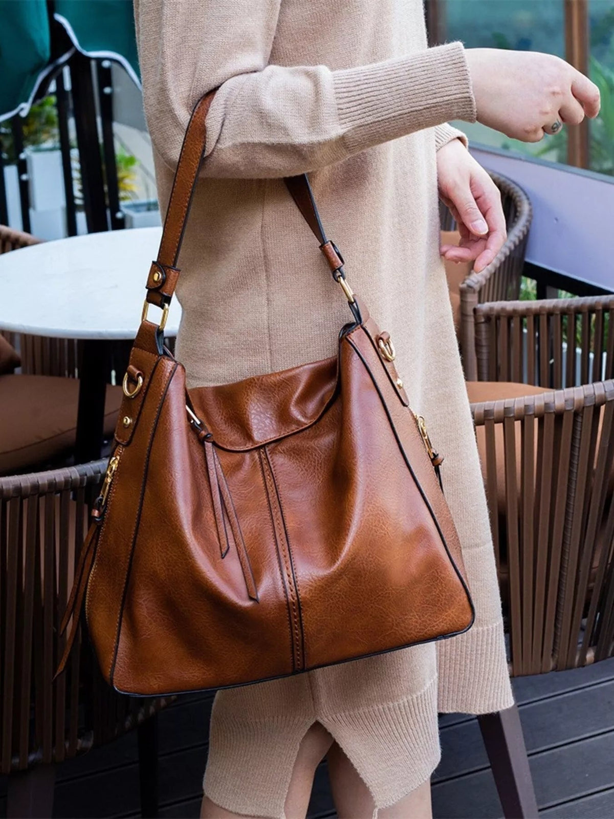 A model carries a medium brown PU leather tote bag with a soft structured silhouette, adjustable shoulder straps, stitched panels, and gold-tone hardware.