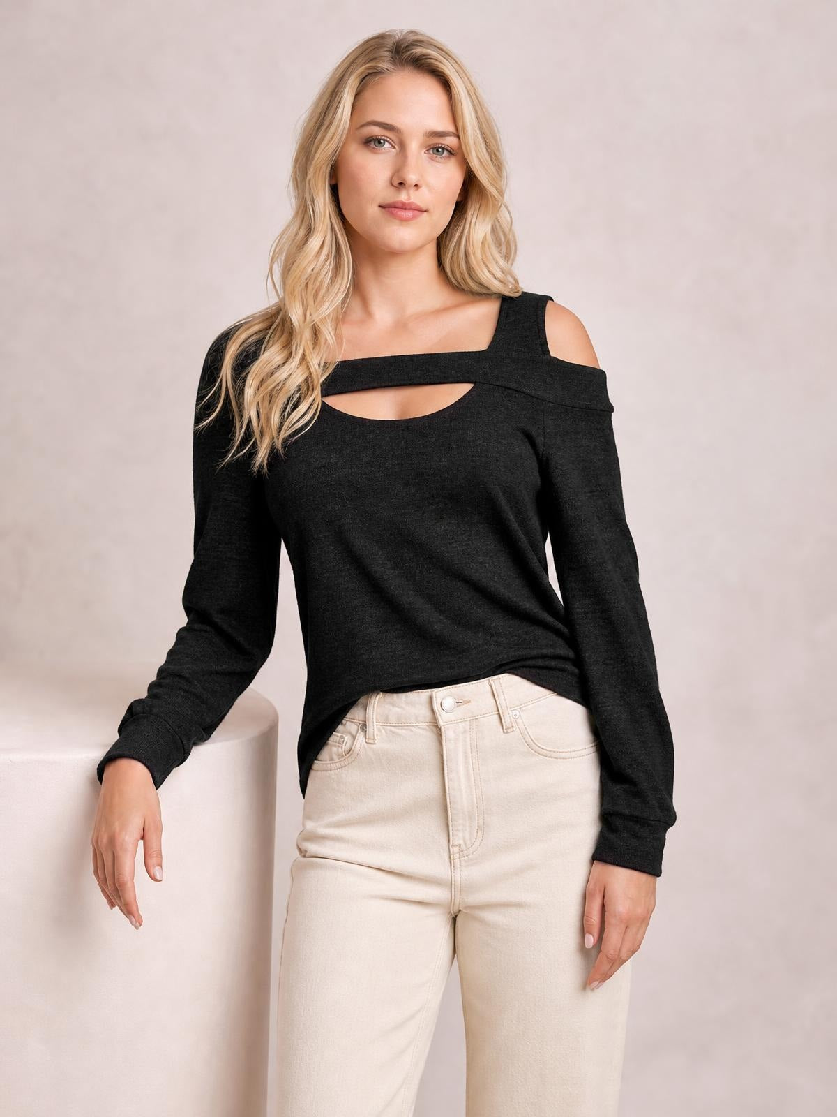 A model wears a black cold shoulder blouse with a square neckline, chest cutout, long sleeves, and a relaxed silhouette while leaning with one hand.