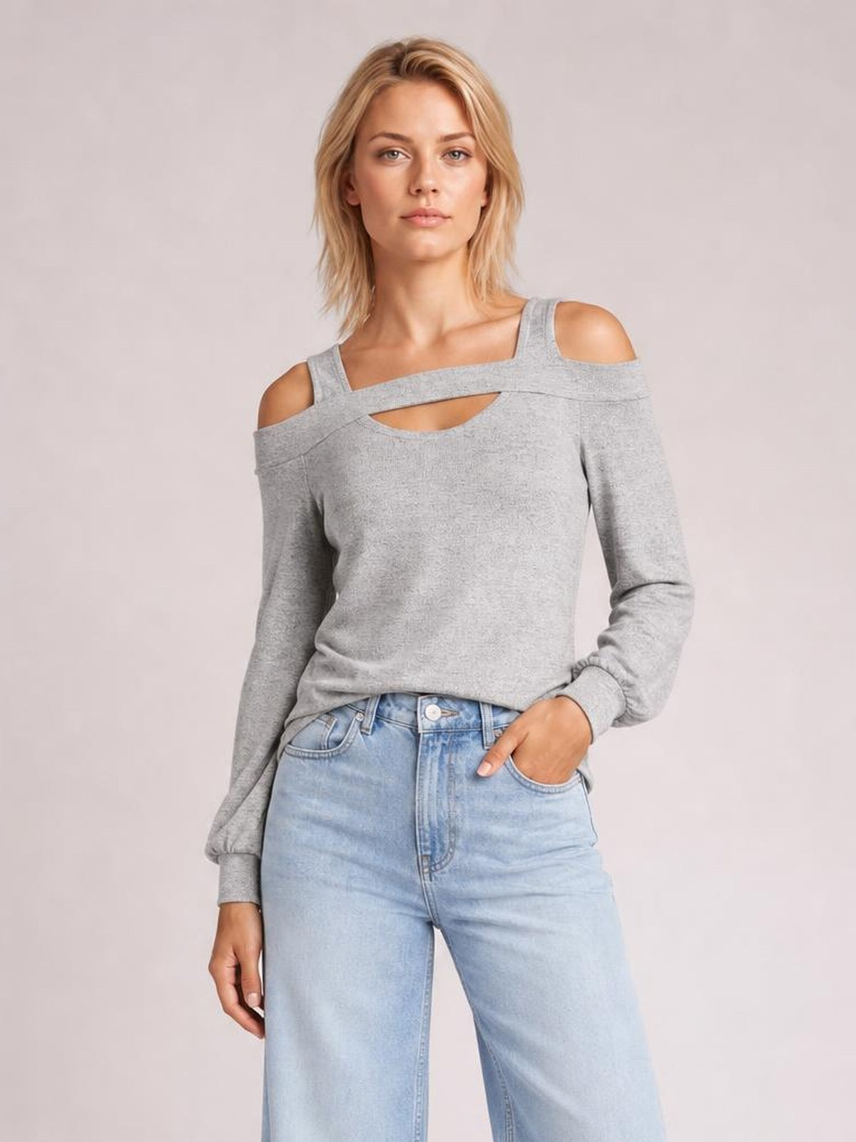 Model poses in a gray cold shoulder blouse with a square neckline, shoulder cutouts, front chest cutout, long sleeves, and a relaxed silhouette.