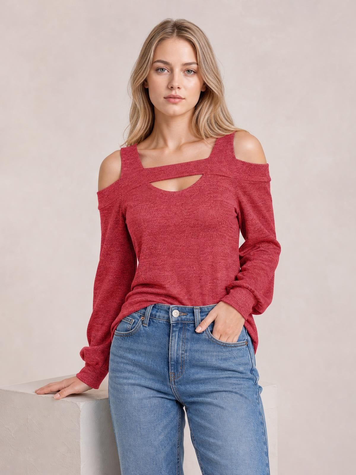 Model wears a red cold-shoulder blouse with a square neckline, chest cutout, long sleeves, and a relaxed silhouette while posing with one hand in her jeans pocket.