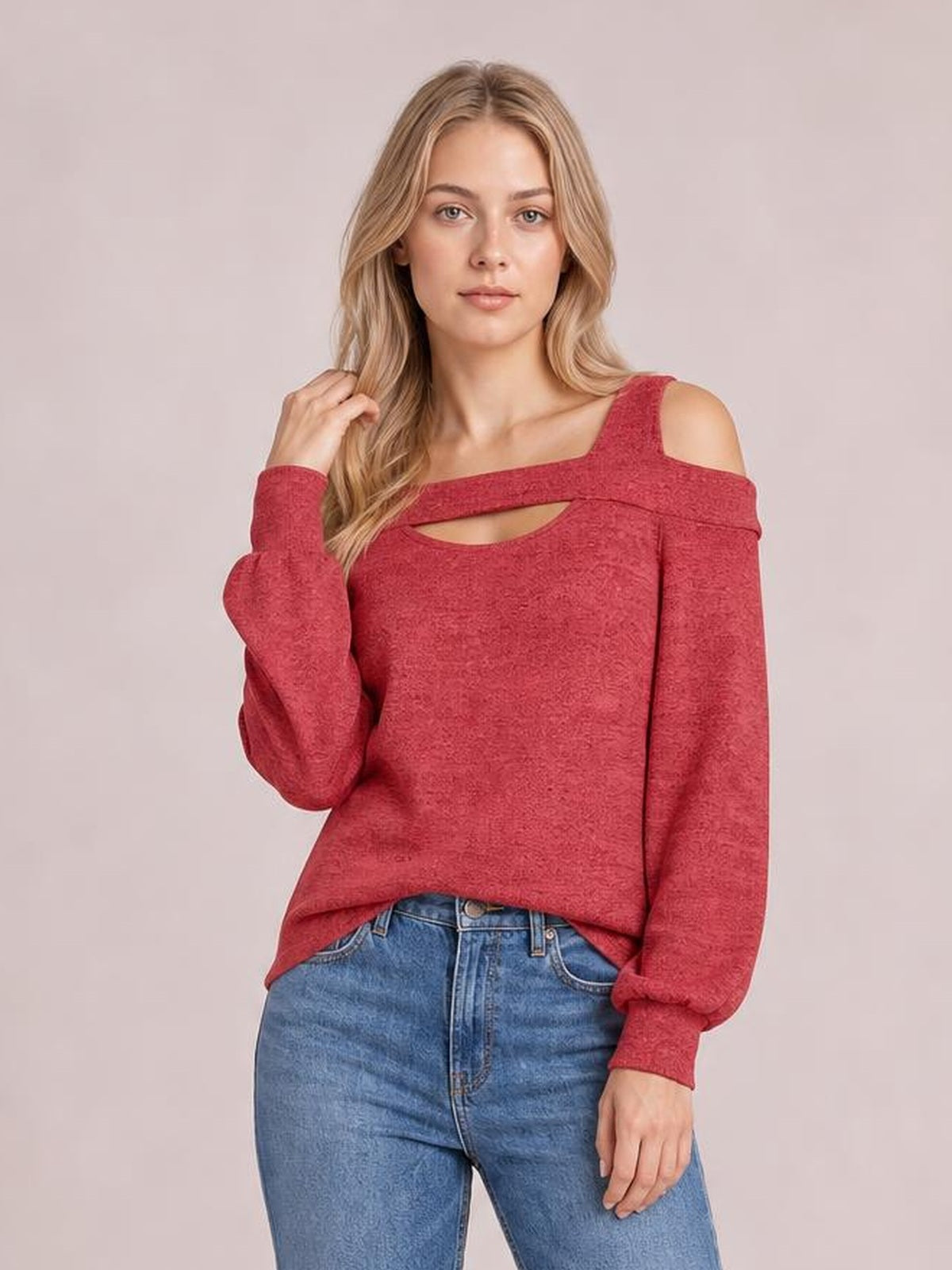 A model poses in a red cold-shoulder blouse with a square neckline, front cutout, long sleeves, and a relaxed silhouette, lifting one hand to her hair.
