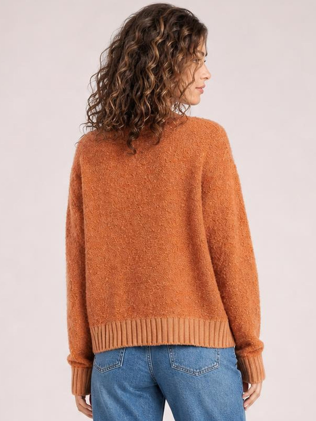 A model turns slightly to show the relaxed silhouette of an orange long-sleeve cardigan with a textured knit, ribbed cuffs, and wide ribbed hem.