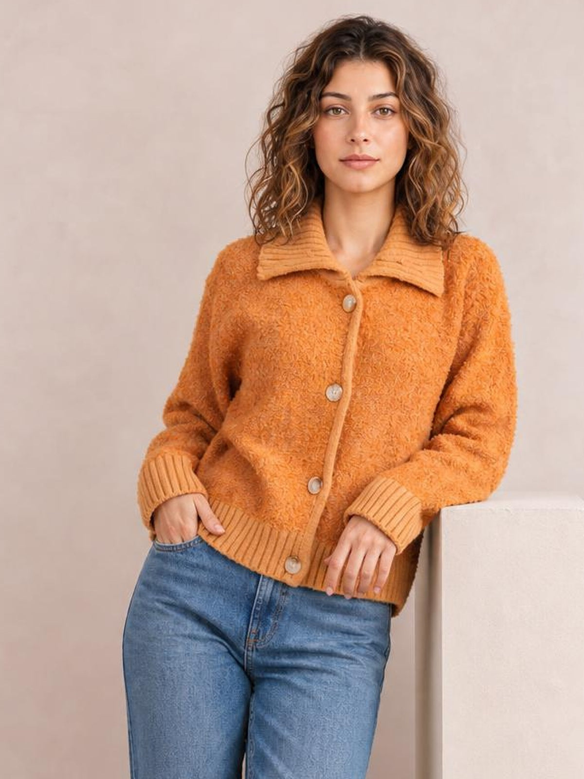 Model poses with hands in her pockets wearing an orange collared button-down cardigan with long sleeves, ribbed cuffs and hem, and a relaxed silhouette.