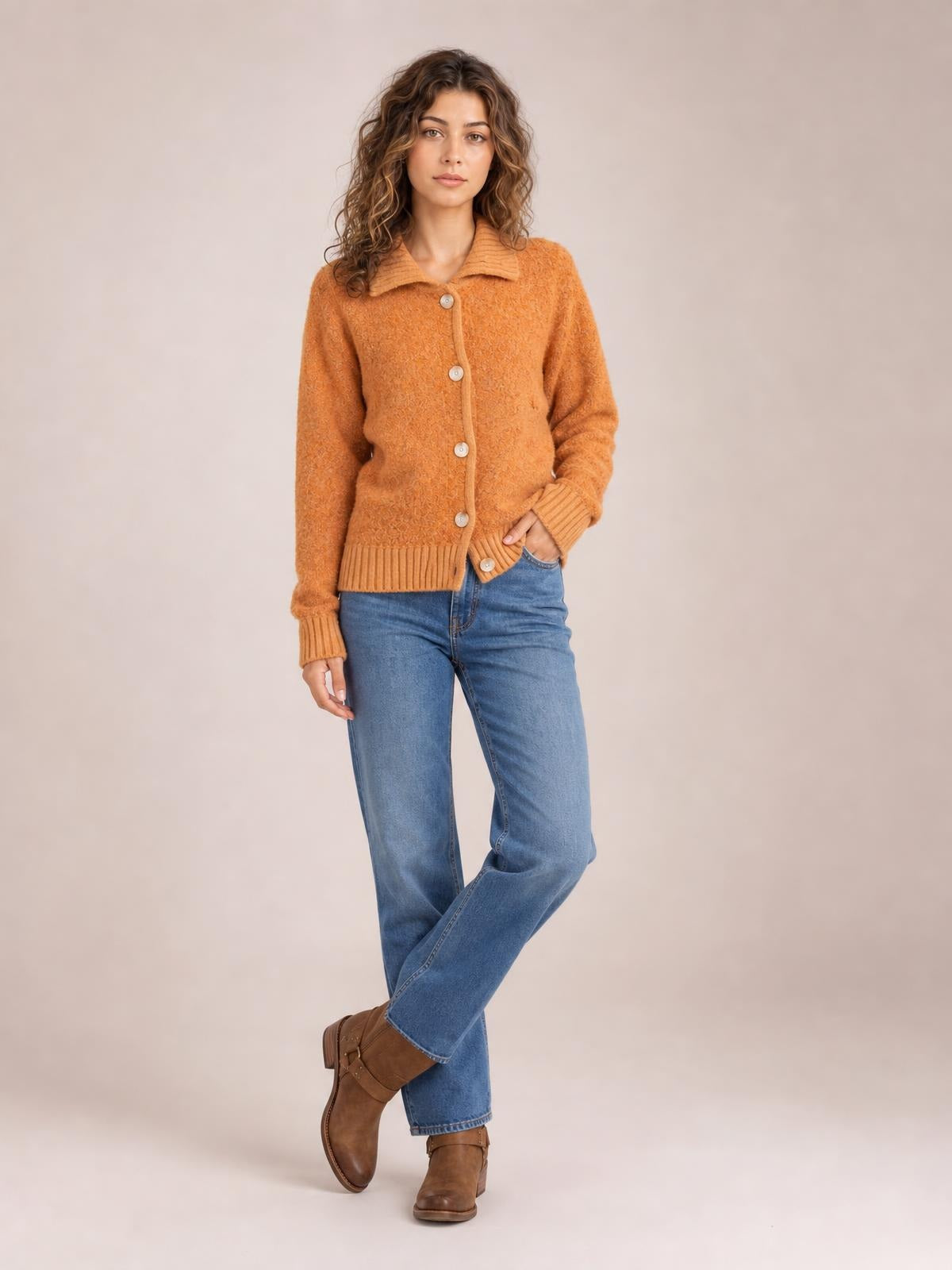Model poses in a rust-orange collared button-down cardigan with long sleeves, ribbed cuffs and hem, a soft textured knit, and a neat relaxed fit.