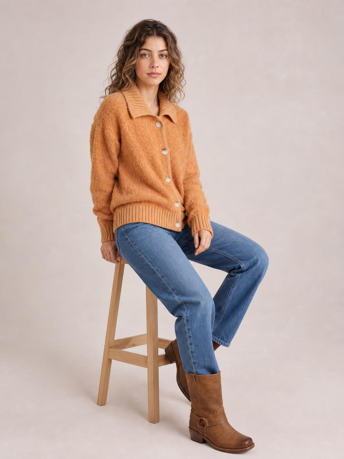 Seated model wears a burnt-orange fuzzy knit cardigan with a ribbed collar, button-down front, long sleeves, ribbed cuffs, and a relaxed silhouette.