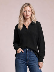 Model in a relaxed pose wears a black cable-knit blouse with a Johnny collar, long regular sleeves, ribbed cuffs, and a loose regular-length silhouette.