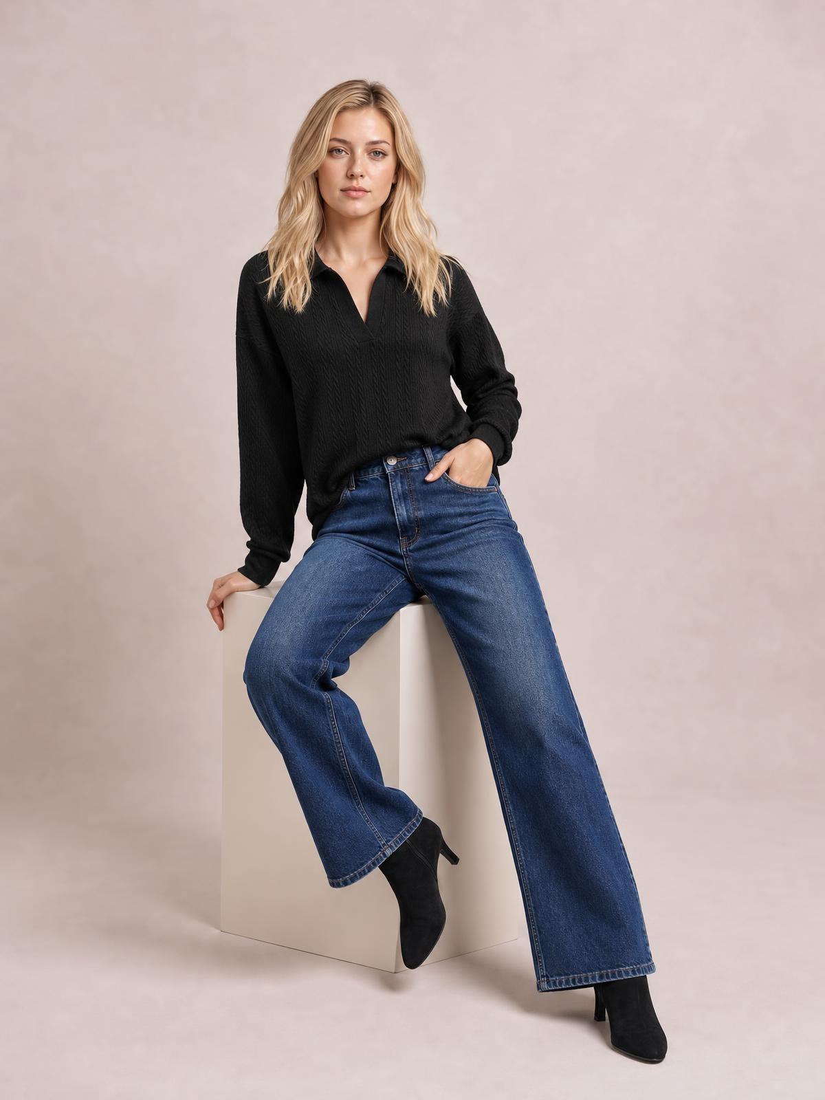 A model sits wearing a black cable-knit blouse with a Johnny collar, V-neck opening, long sleeves, ribbed cuffs, and a relaxed regular-length silhouette.