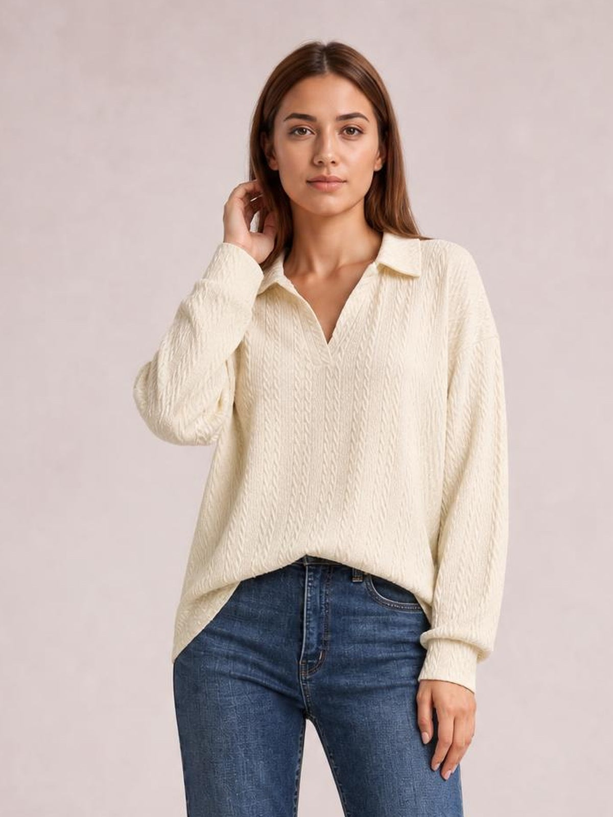 Model wears an ivory cable-knit blouse with a Johnny collar, long sleeves, relaxed regular silhouette, and ribbed cuffs while touching her hair.