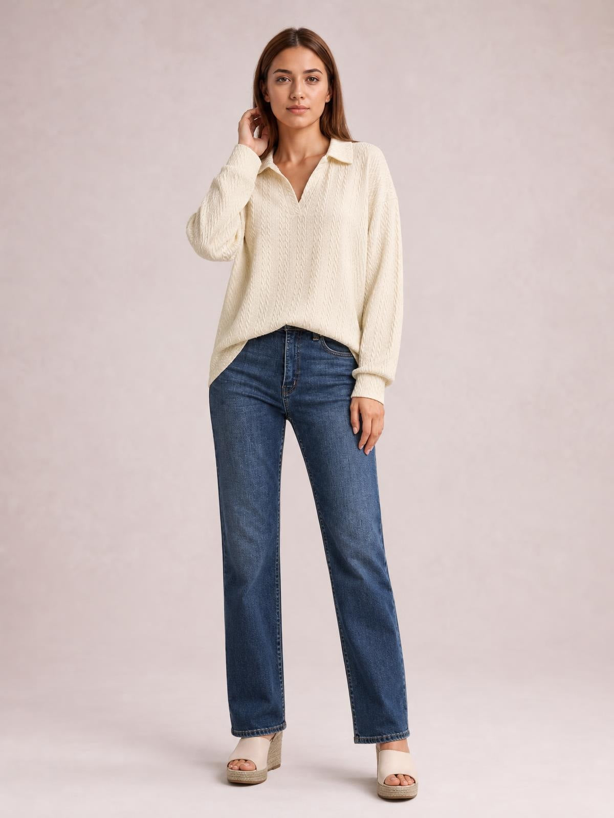 Model poses in a cream cable-knit blouse with a Johnny collar, long sleeves, and a relaxed regular silhouette, lightly touching her hair.