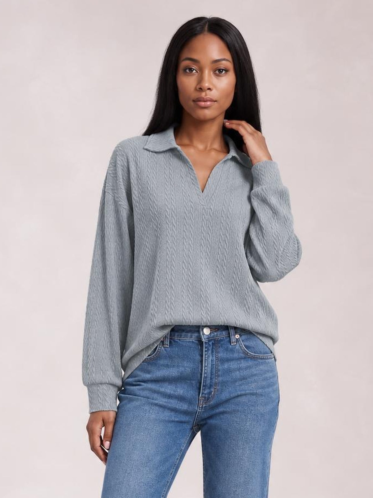 Model wears a gray cable-knit blouse with a Johnny collar, V-neck opening, long sleeves, and a relaxed regular-length silhouette while touching her hair.