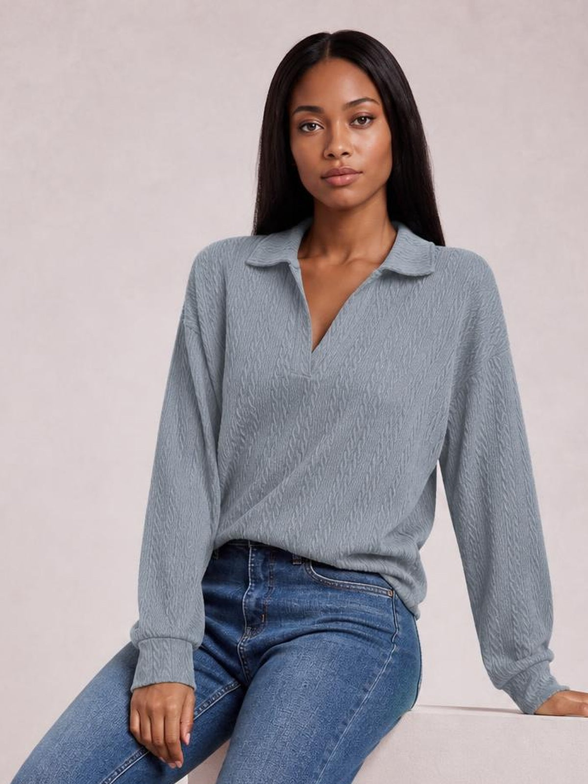 A seated model wears a blue-gray textured blouse with a Johnny collar, V-neck opening, long sleeves, ribbed cuffs, and a relaxed regular silhouette.
