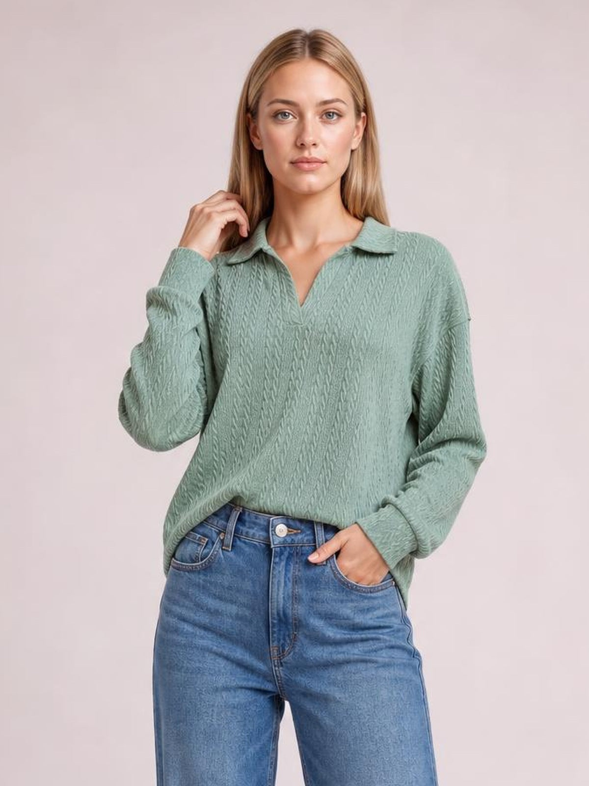 A model poses in a sage green cable-knit blouse with a collared Johnny neckline, long sleeves, relaxed silhouette, and ribbed cuffs.
