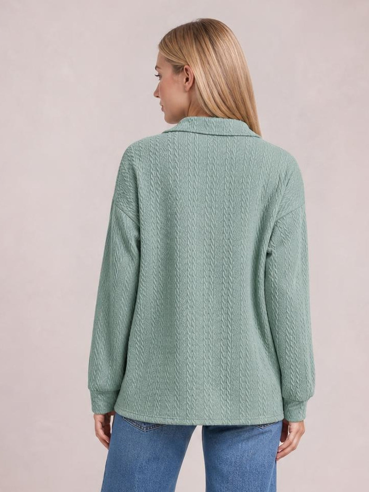A model stands turned away in a sage green cable-knit blouse with a Johnny collar, long sleeves, ribbed cuffs, and a relaxed regular-length silhouette.