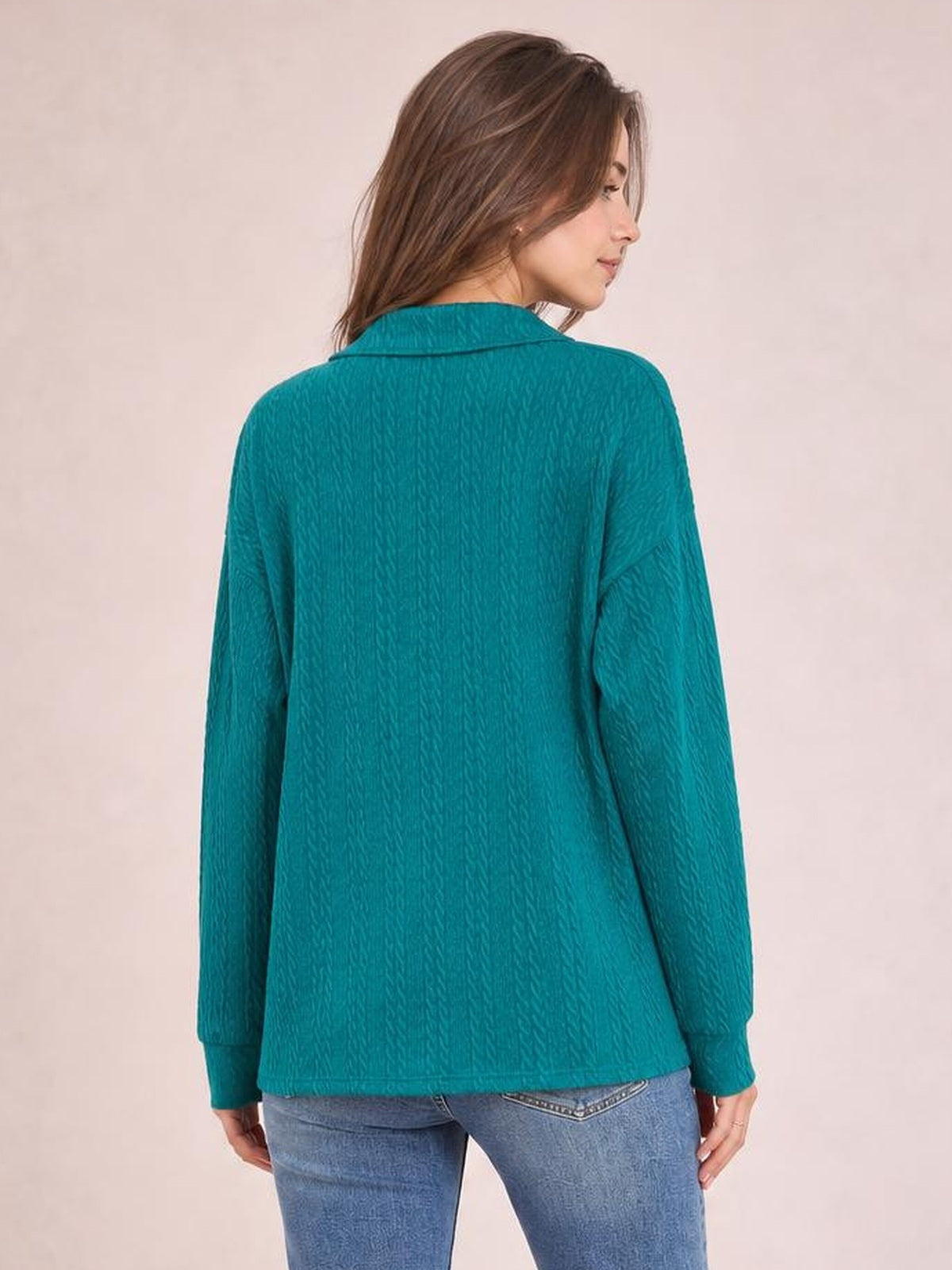 A model shown from the back wears a teal solid cable-knit blouse with a collared neckline, long sleeves, cuffs, and a relaxed regular-length silhouette.