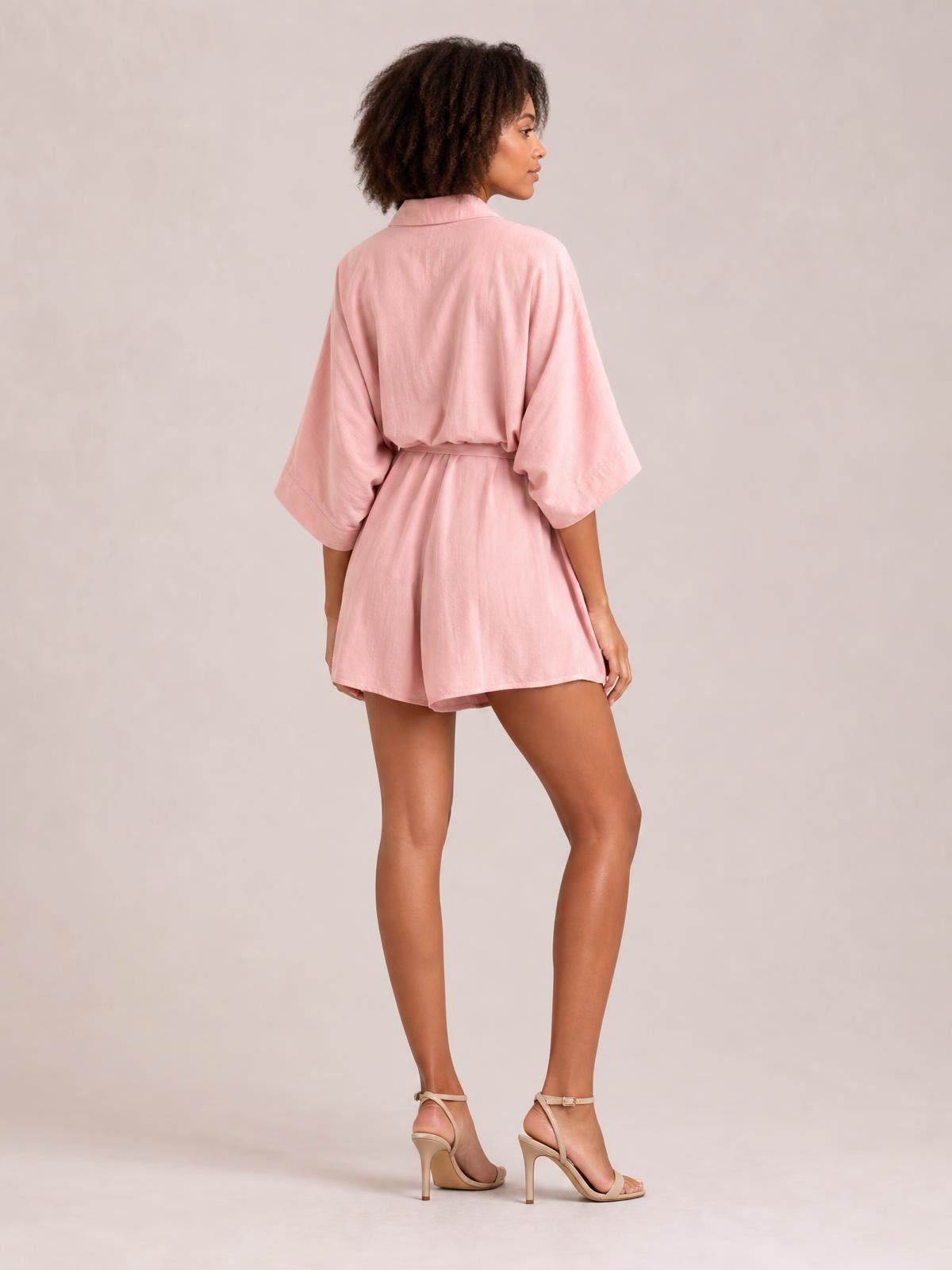 Model shown from the back in a pink collared neck half-sleeve romper with a tied waist, relaxed fit, and flared shorts silhouette.
