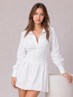 Model poses in a white collared mini dress with long lantern sleeves, ruched corset-style waist, gathered skirt, and relaxed A-line silhouette.