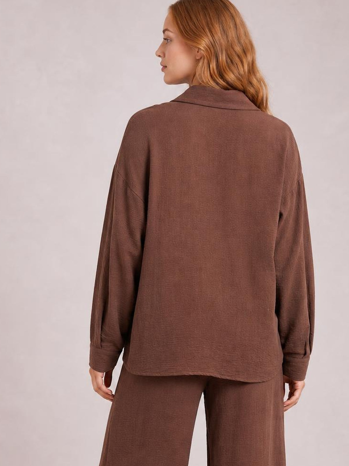 Model shown from behind wearing a brown collared long-sleeve top and matching pants set with a relaxed silhouette, cuffed sleeves, and straight-leg construction.