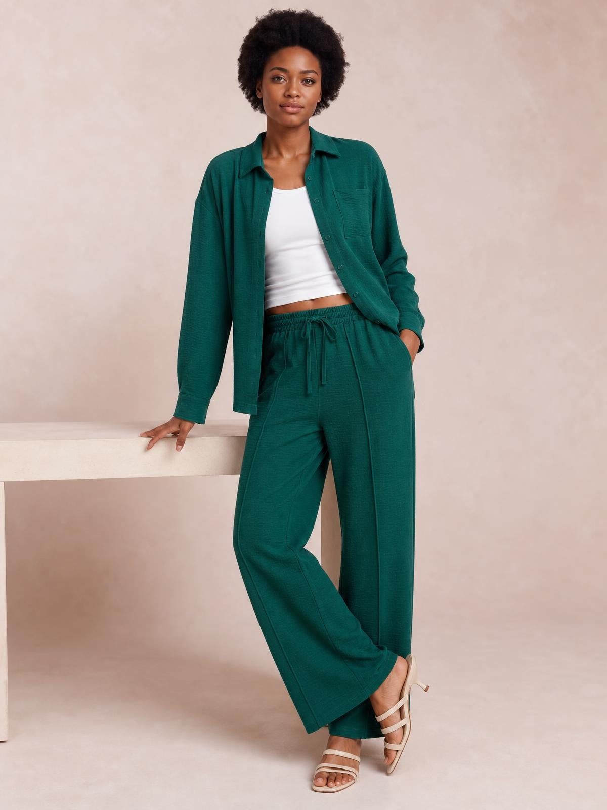 Model poses in a teal collared long-sleeve top and matching wide-leg pants with buttoned front, chest pocket, drawstring waist, and relaxed silhouette.