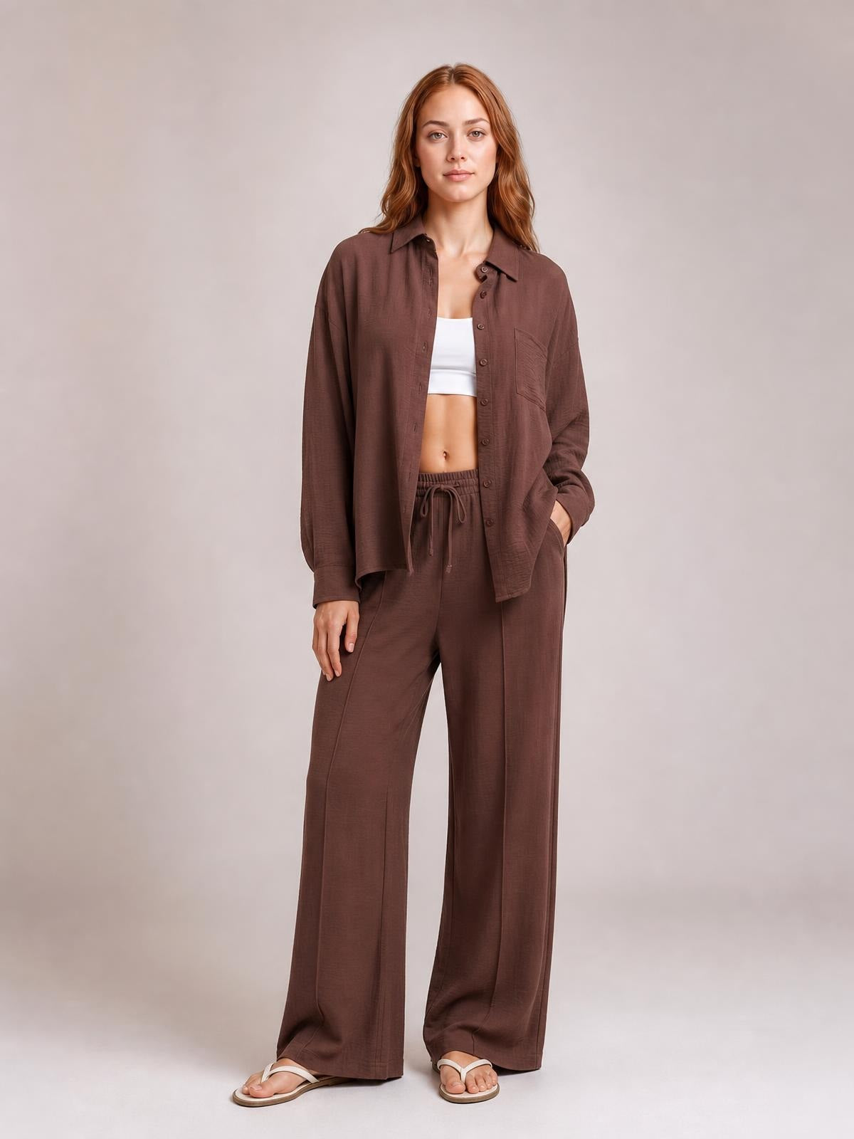 A model poses in a brown collared long-sleeve button-front top and matching wide-leg drawstring pants with a chest pocket and side pockets.