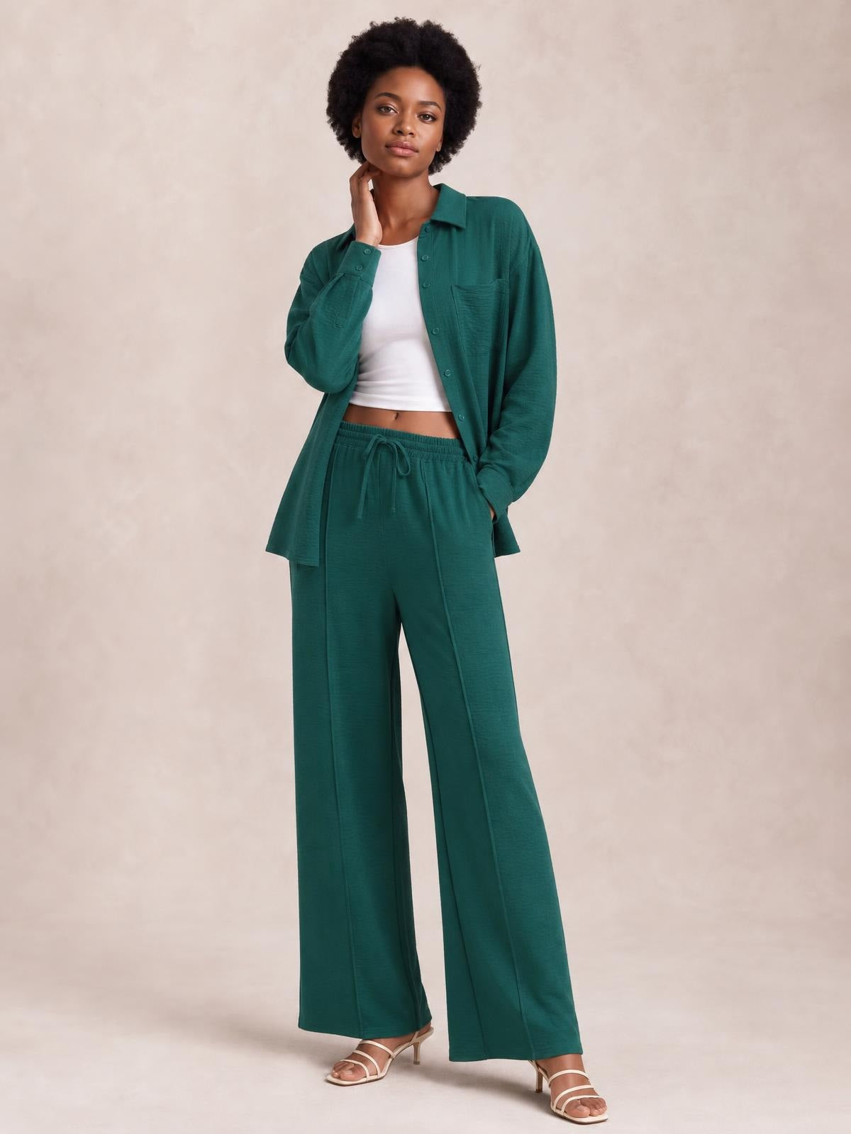 A model poses in a teal collared long-sleeve button-front top and matching wide-leg drawstring pants with pockets, one hand at her neck.
