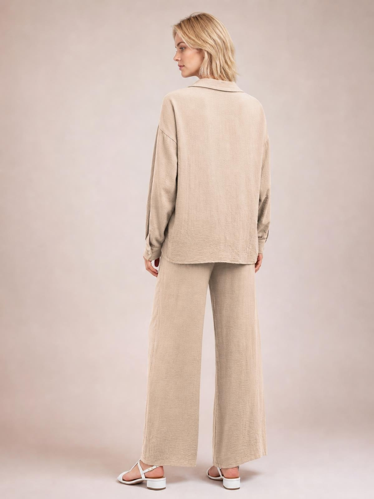 A model stands in a relaxed pose wearing a beige collared long-sleeve top and matching wide-leg pants with a loose, streamlined silhouette.
