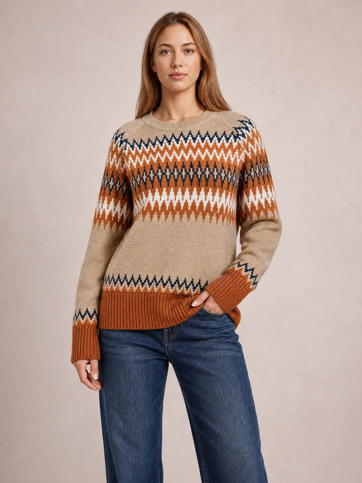 Model poses in a beige color block crew neck sweater with orange, white, and navy geometric knit bands, ribbed cuffs and hem, and a relaxed silhouette.