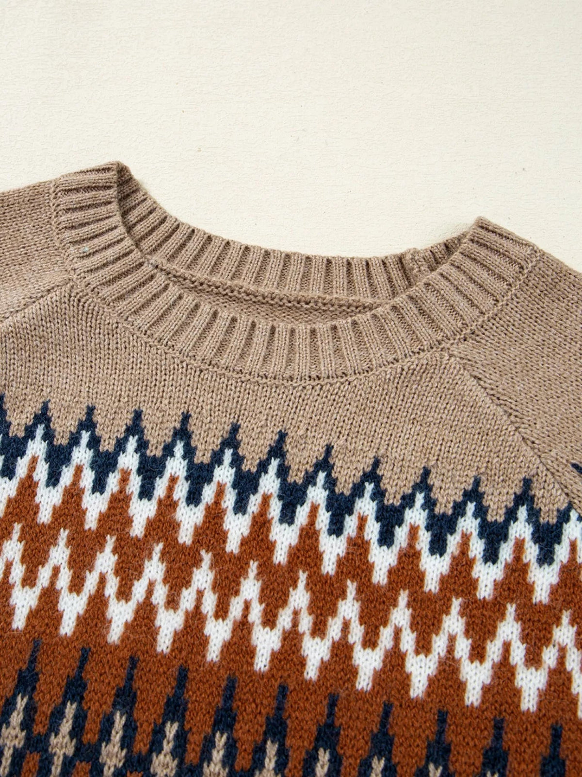 Close-up of a color block crew neck sweater featuring a ribbed neckline and geometric knit pattern in tan, rust, navy, and white.