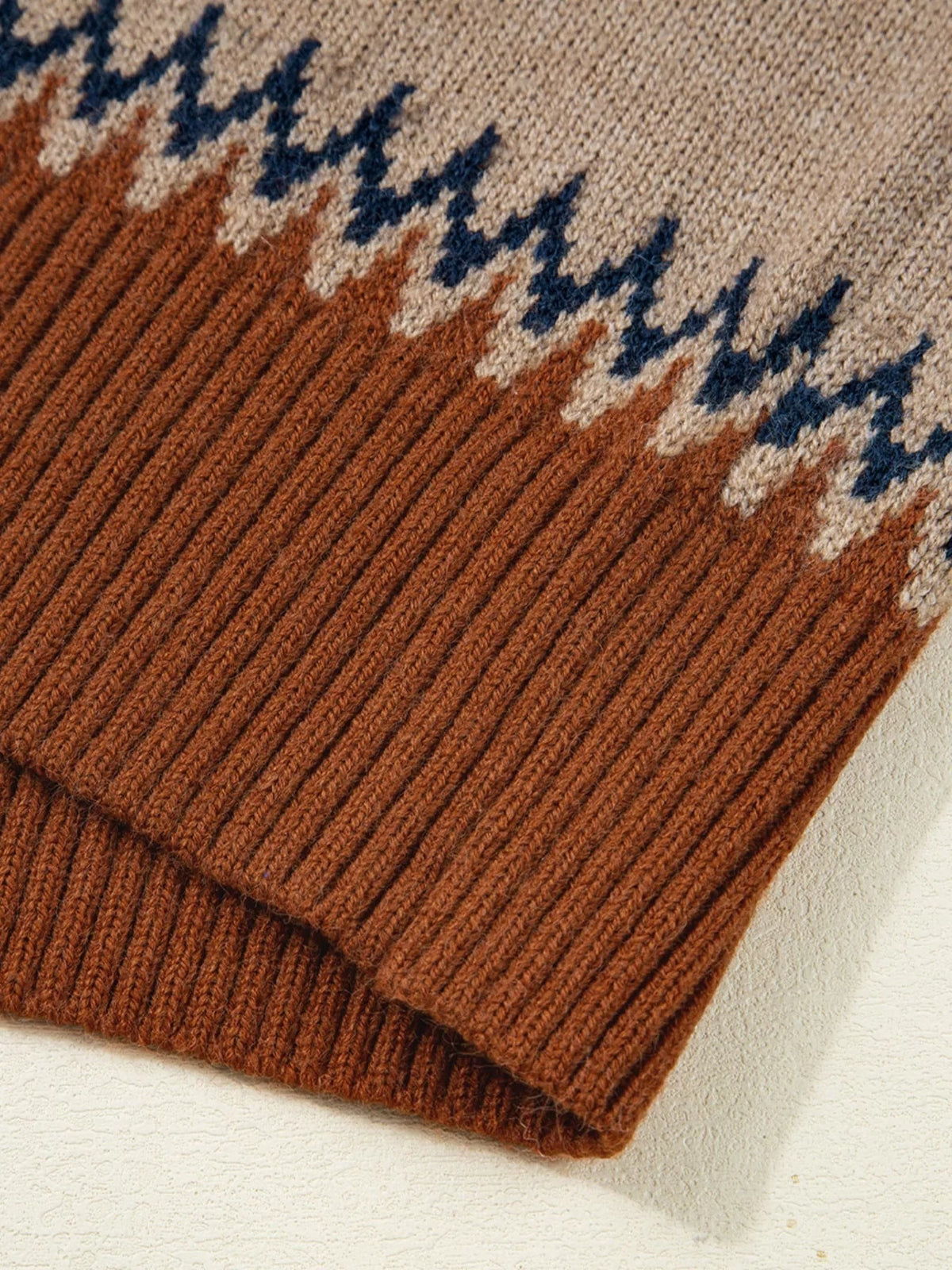 Close-up shows a brown rib-knit sweater hem with cream and navy geometric color-block detailing and a softly textured knit construction.