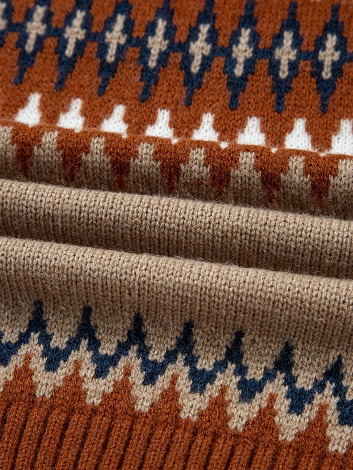 Close-up of a color block sweater knit in rust, navy, cream, and taupe with textured geometric patterning and wide ribbed construction.