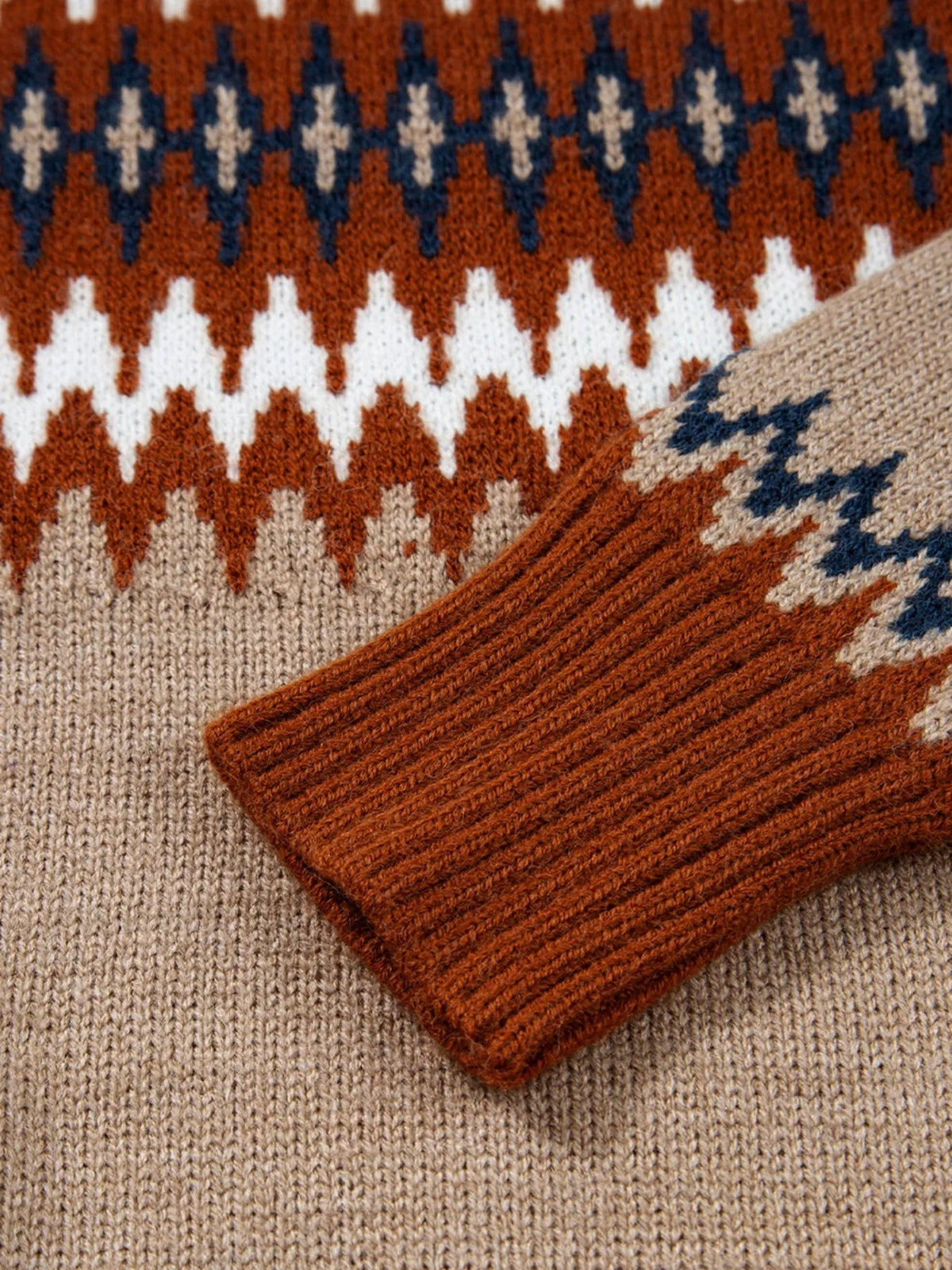 Close-up of a color block sweater knit in rust brown, cream, and navy, showing geometric patterning and a ribbed cuff with textured construction.